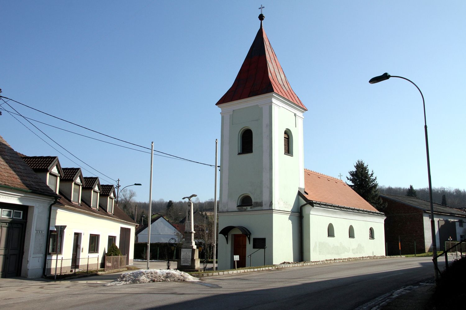 Kostel s červenou střechou a věží ve vesnici pod jasnou oblohou.