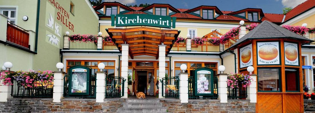 Vchod do restaurace Kirchenwirt s květinami a nápisy.