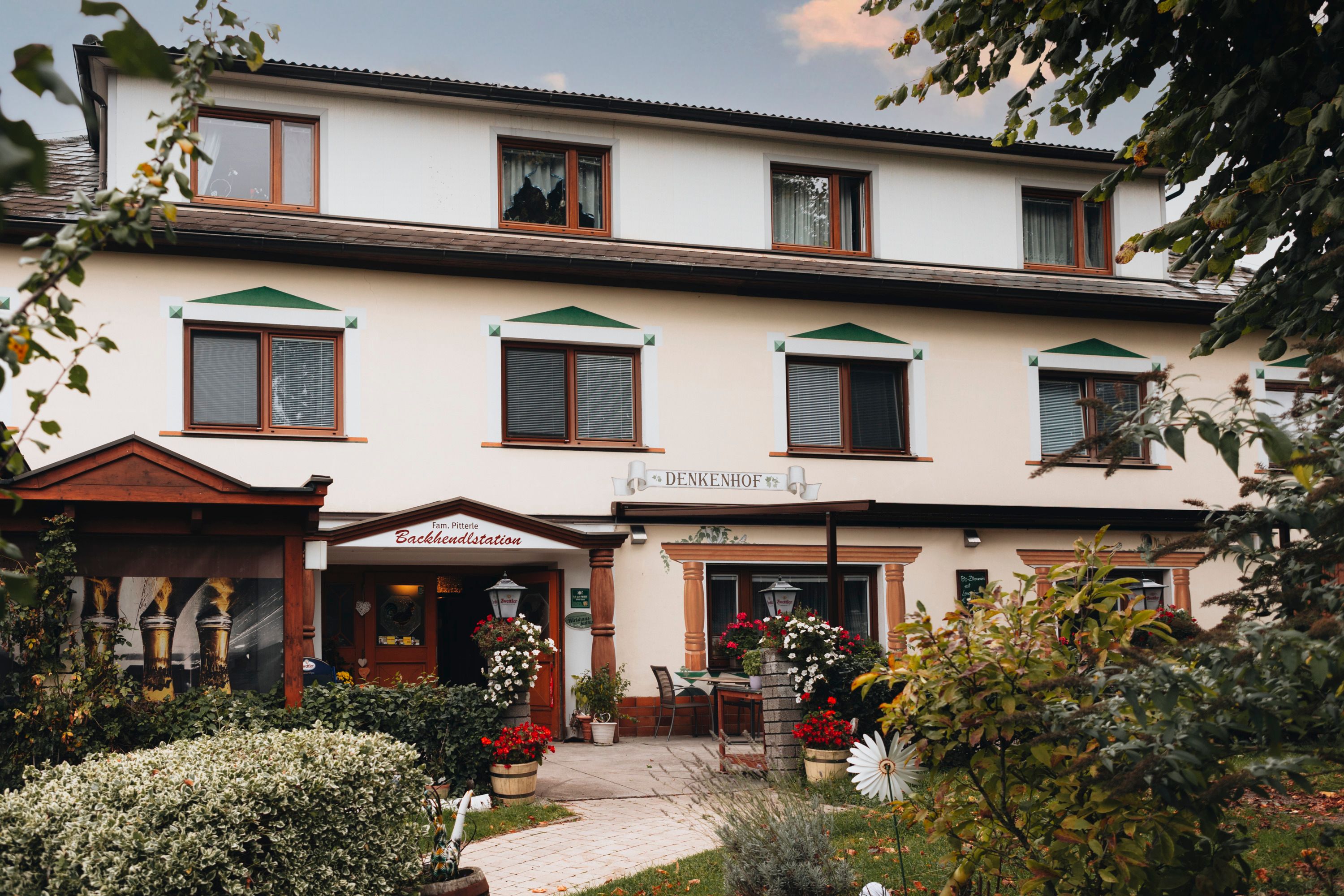 Tradiční hostinec s květinami a stromy v popředí.