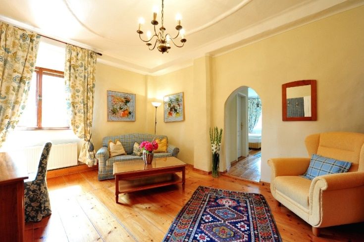 Útulný obývací pokoj s dřevěnou podlahou, pohovkou, křeslem, kobercem a květinami.