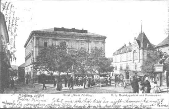 Historický pohled na hotel Stadt Mödling s lidmi a kočáry na ulici.