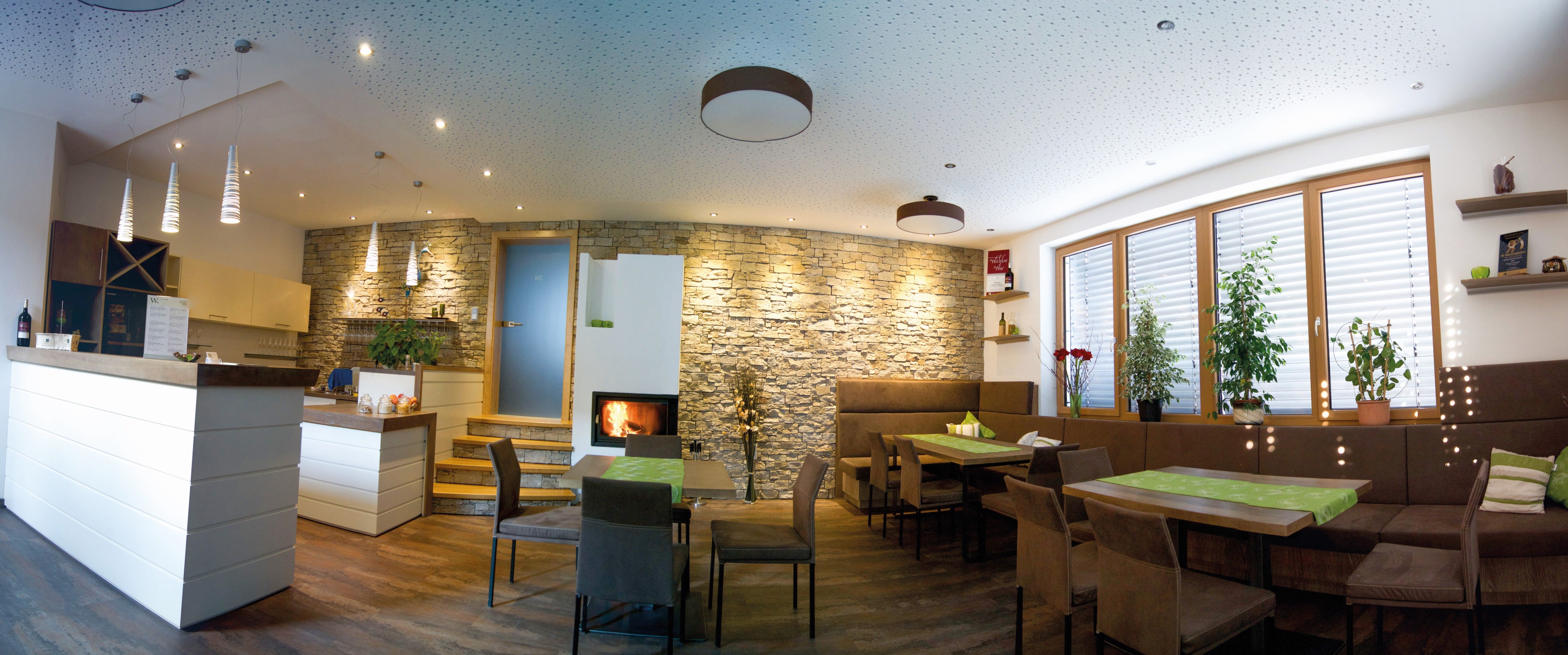 Moderní degustační místnost s dřevěným nábytkem, kamennou stěnou, krbem a rostlinami.