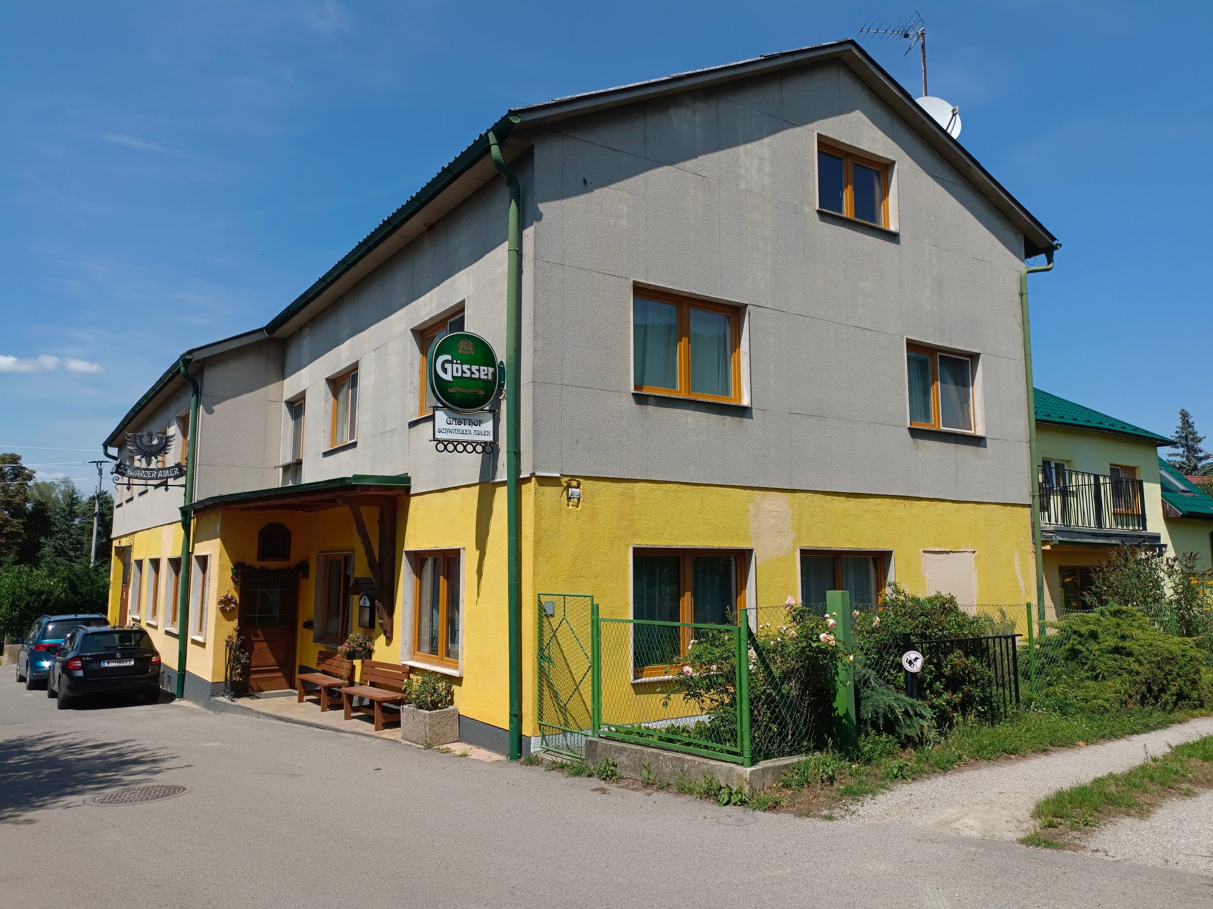 Pohled zvenčí na žlutošedý hostinec s nápisem Gösser a zaparkovanými auty.