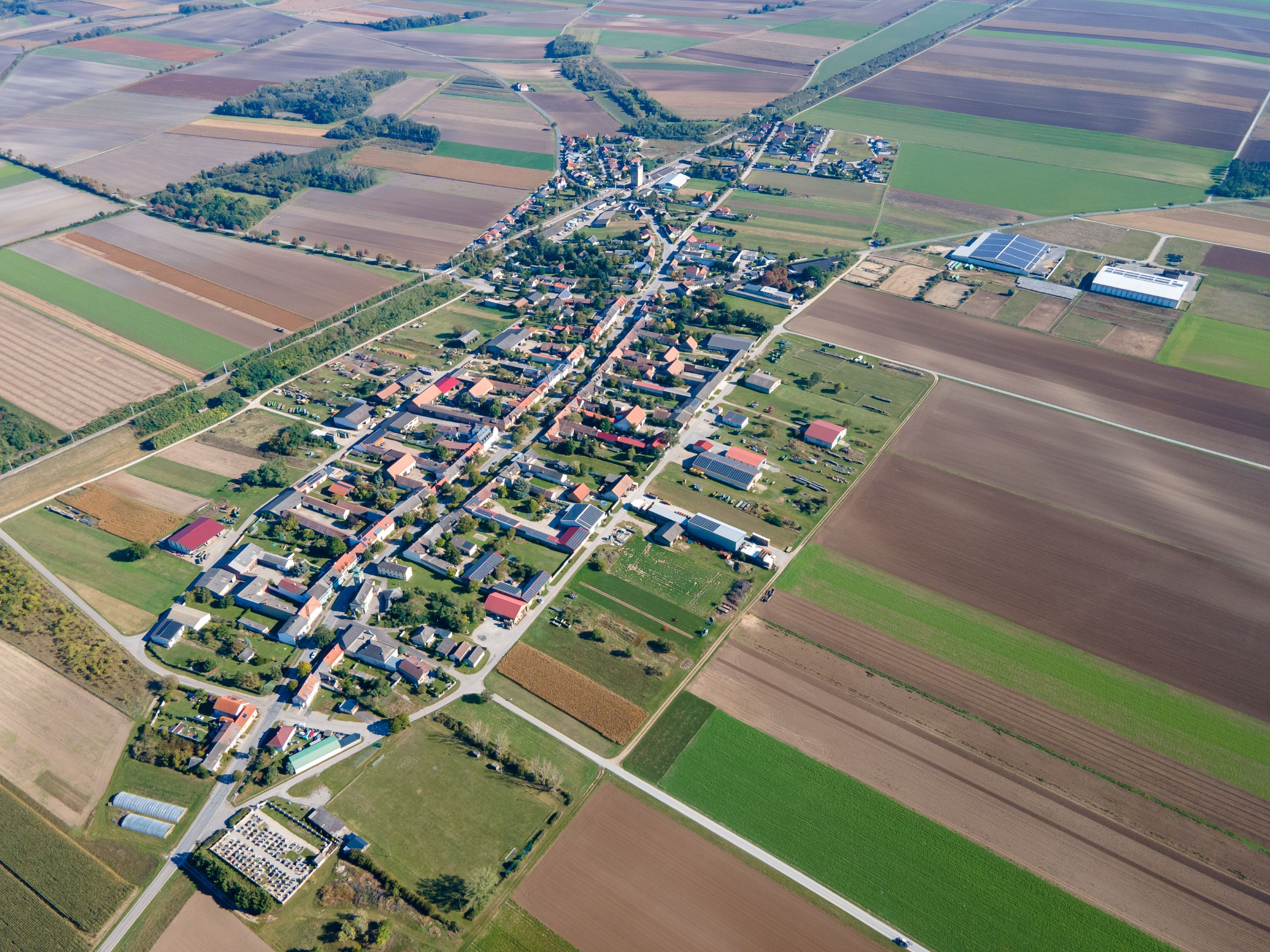 Letecký snímek obce Weiden an der March s hustě zastavěným centrem, obklopeným poli a zemědělskou půdou.
