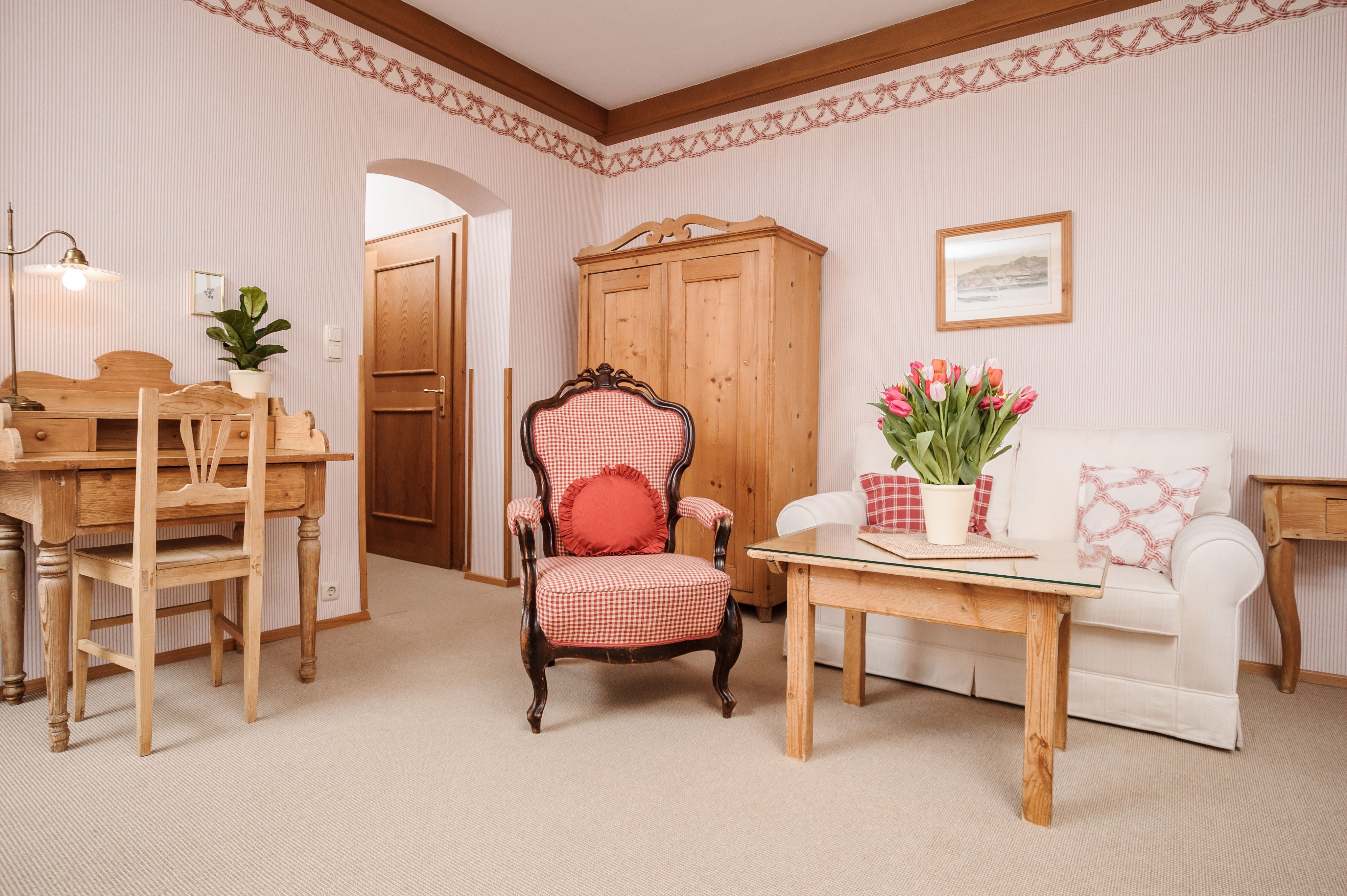 Útulný obývací pokoj s dřevěným nábytkem, křeslem, pohovkou a stolem s tulipány.