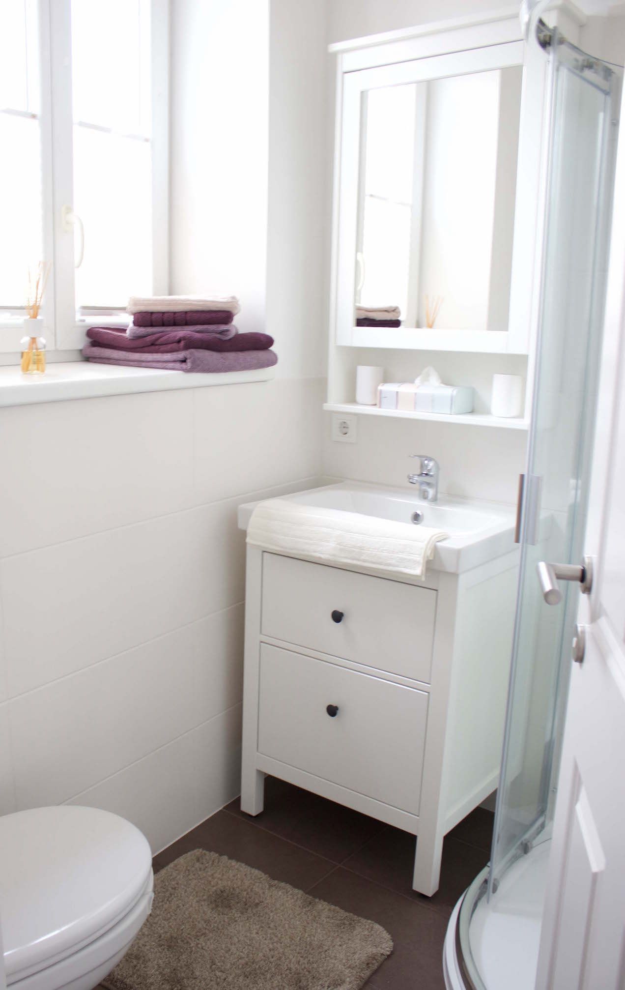 Moderní koupelna s bílým umyvadlem, zrcadlem, ručníky a sprchou.