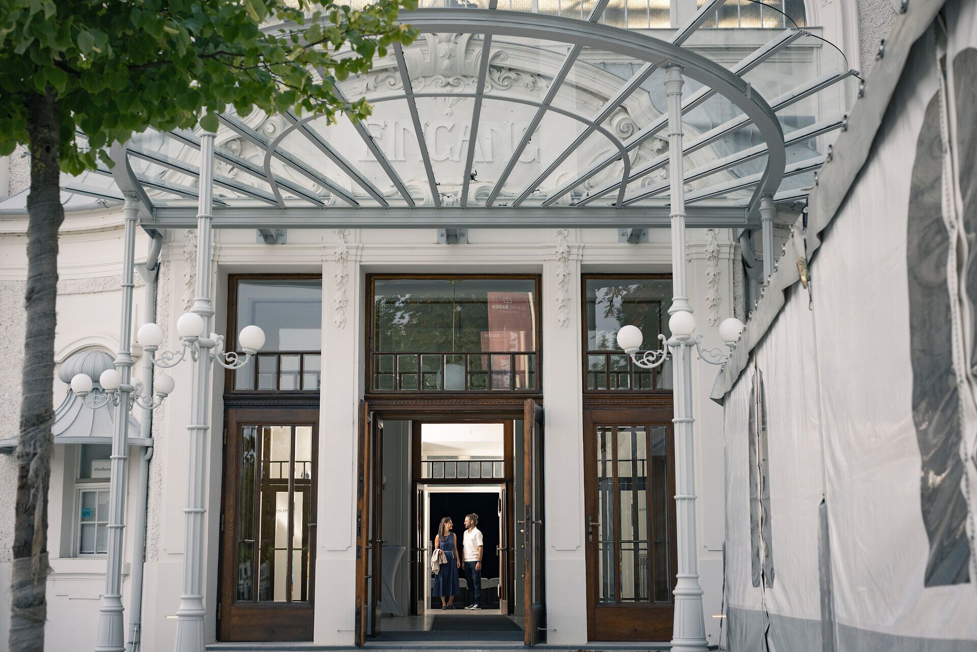 Ein Paar verlässt nach einer Veranstaltung die historische Sommerarena Baden, ein beeindruckendes Bauwerk. 