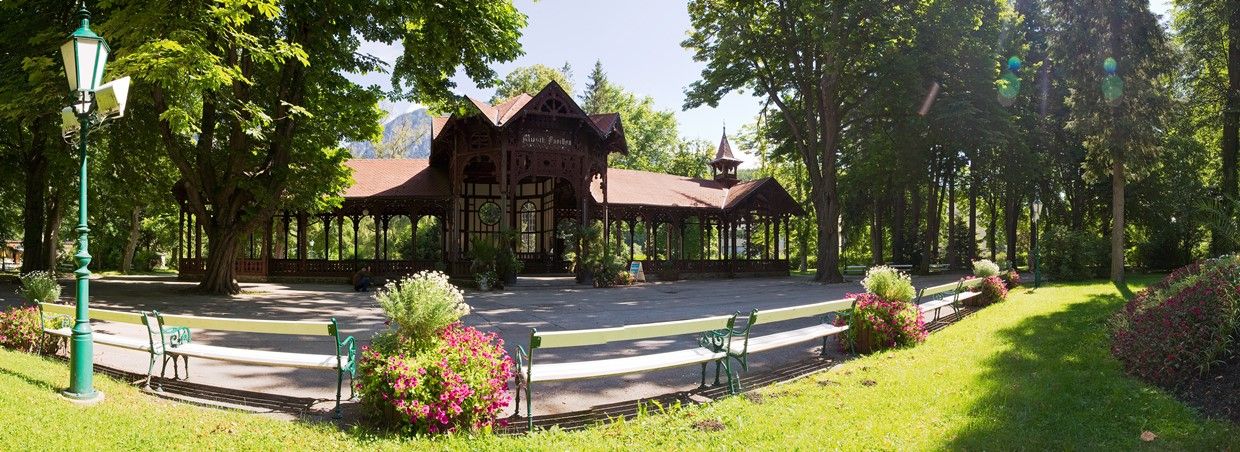 Pavilon v lázeňské zahradě Reichenau, obklopený stromy a květinovými záhony.