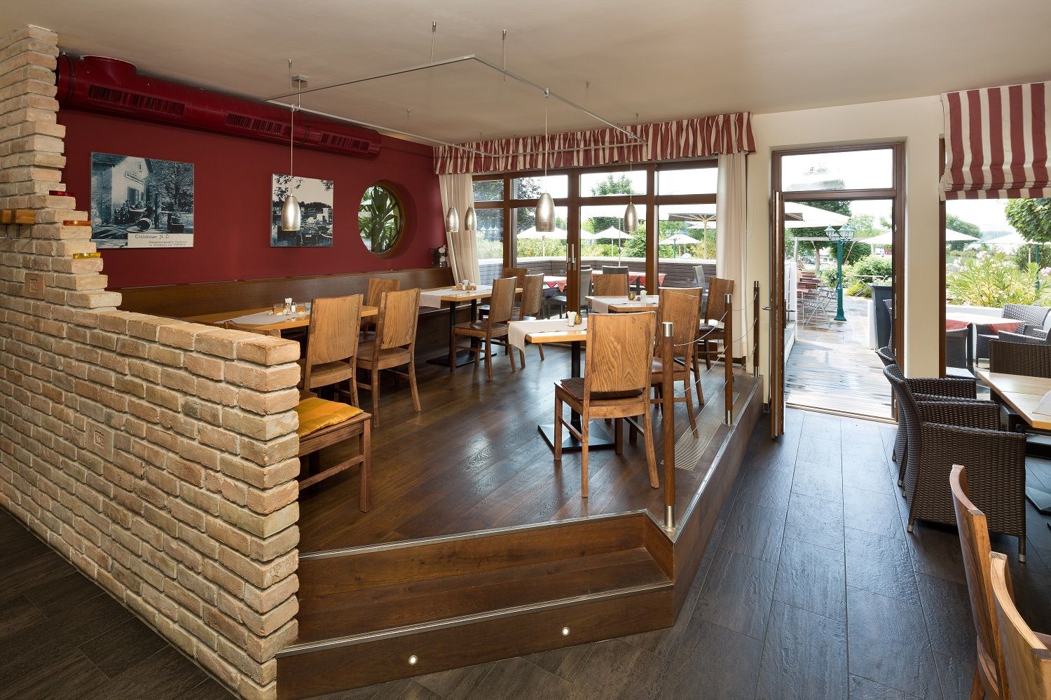 Útulná restaurace s dřevěným nábytkem, červenými stěnami a velkými okny vedoucími na terasu.