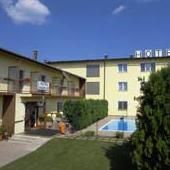 Pohled na žlutý hotel s bazénem a zahradou zvenčí.