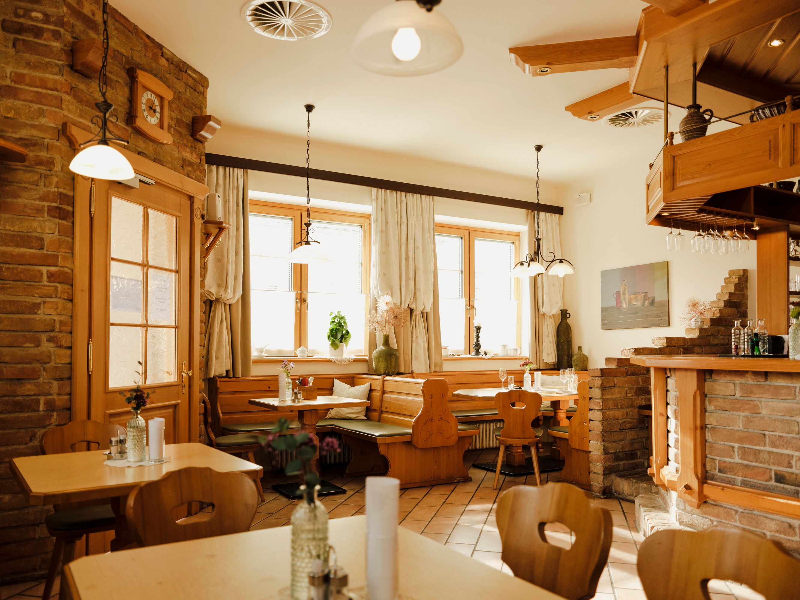 Útulná jídelna s dřevěným nábytkem a cihlovými stěnami, zdobená rostlinami a lampami.