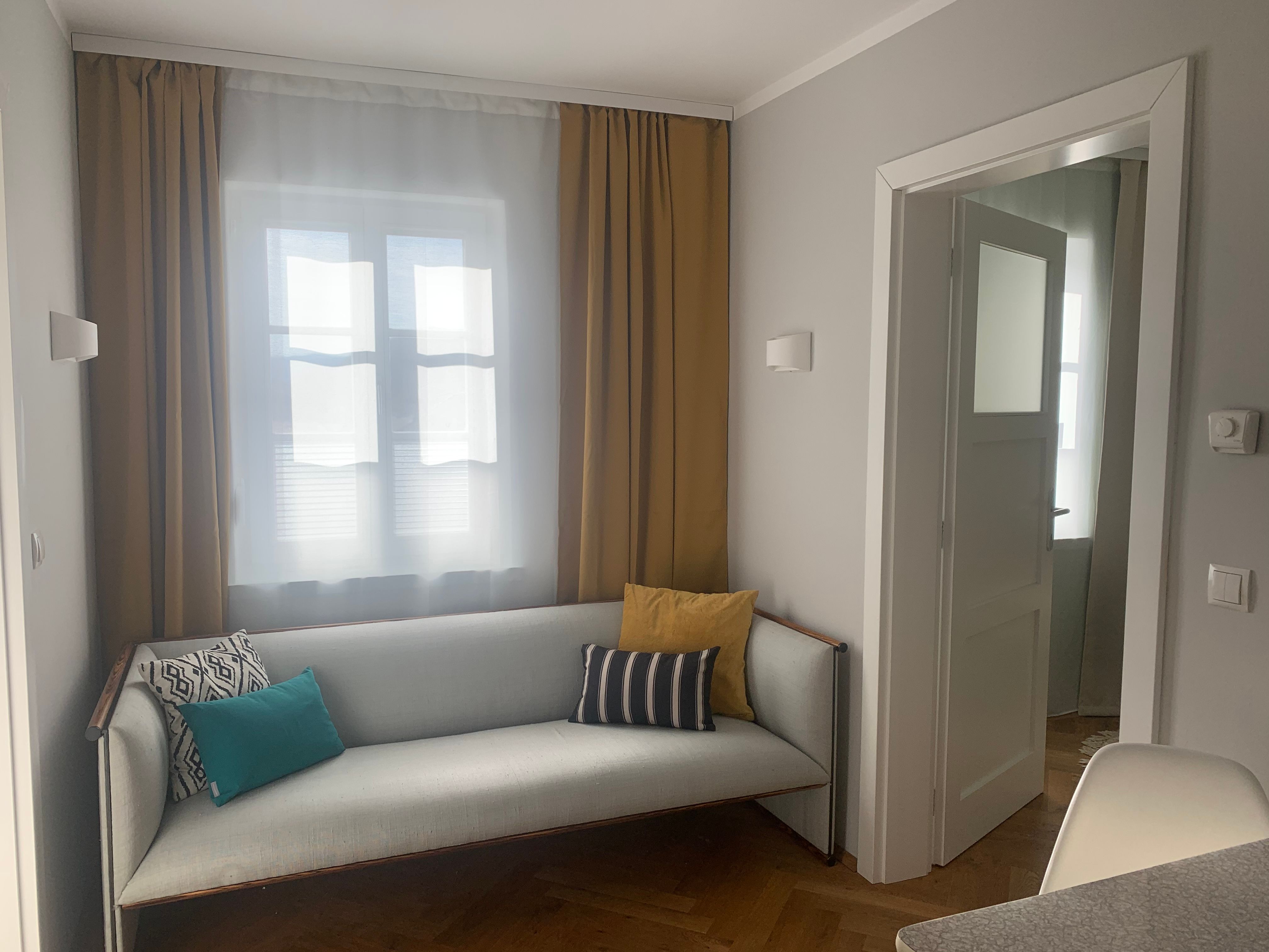 Útulný obývací pokoj s pohovkou a polštáři, žlutými závěsy a otevřenou zárubní.