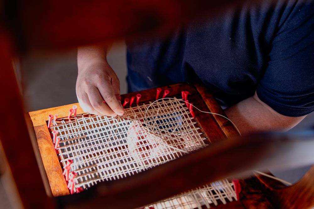 Osoba opravuje židli Thonet s vídeňským proutím.