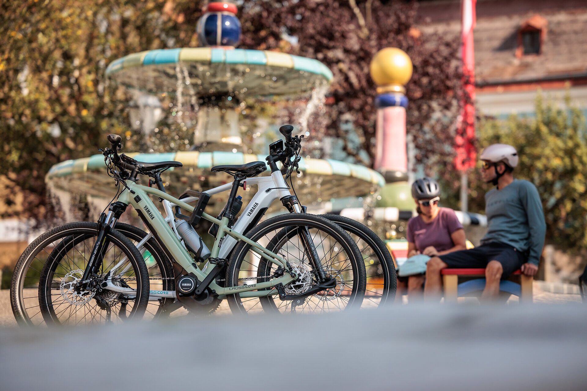 Cyklisté odpočívají na hřejivém slunci u Hundertwasserovy fontány, obklopeni bublající vodou a barevnými rostlinami. Čerstvý vzduch a malebná scenérie vybízejí k tomu, abyste si vychutnali krásu přírody a načerpali novou energii.