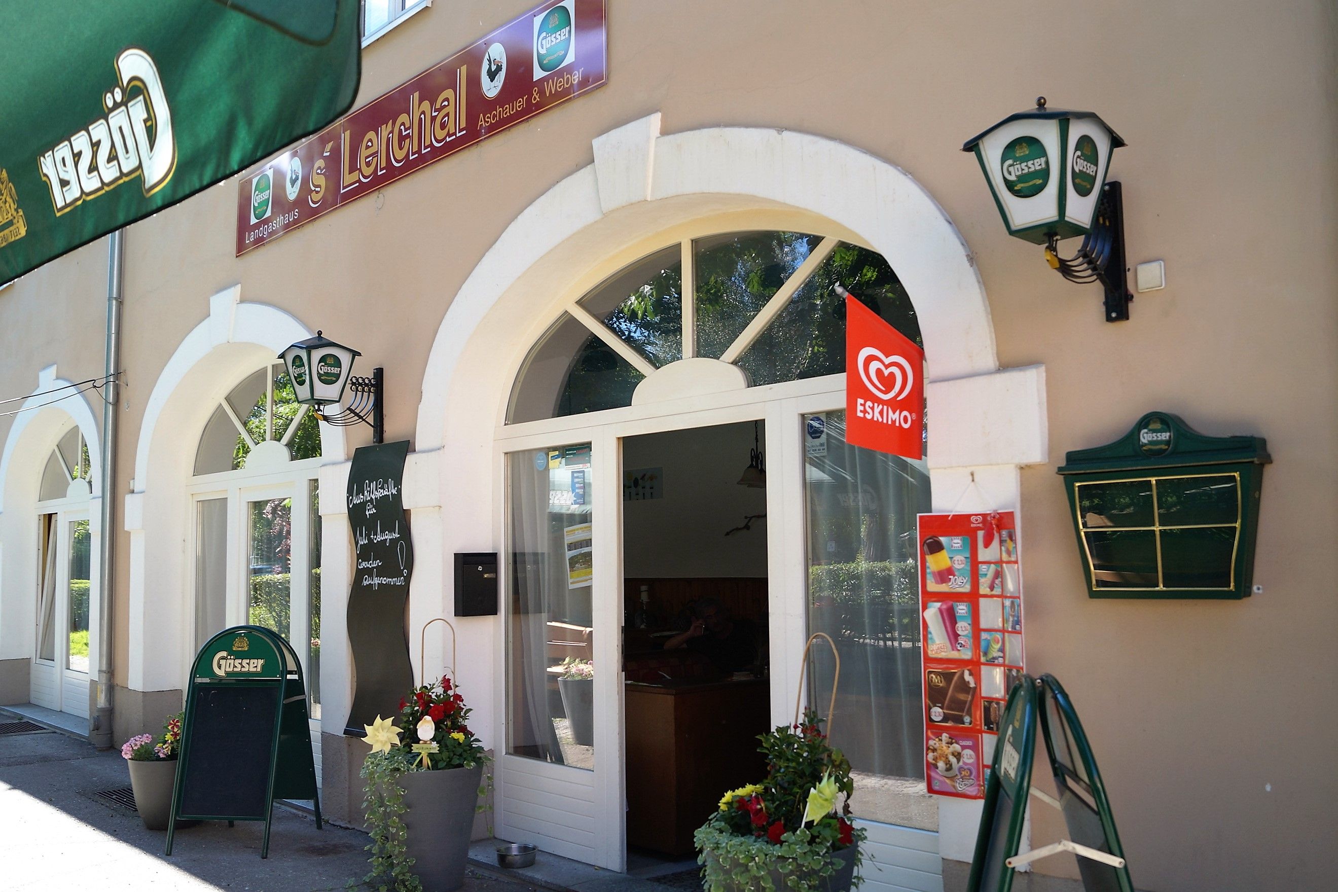 Pohled zvenčí na restauraci s nápisy Gösser a reklamou na eskymáckou zmrzlinu.