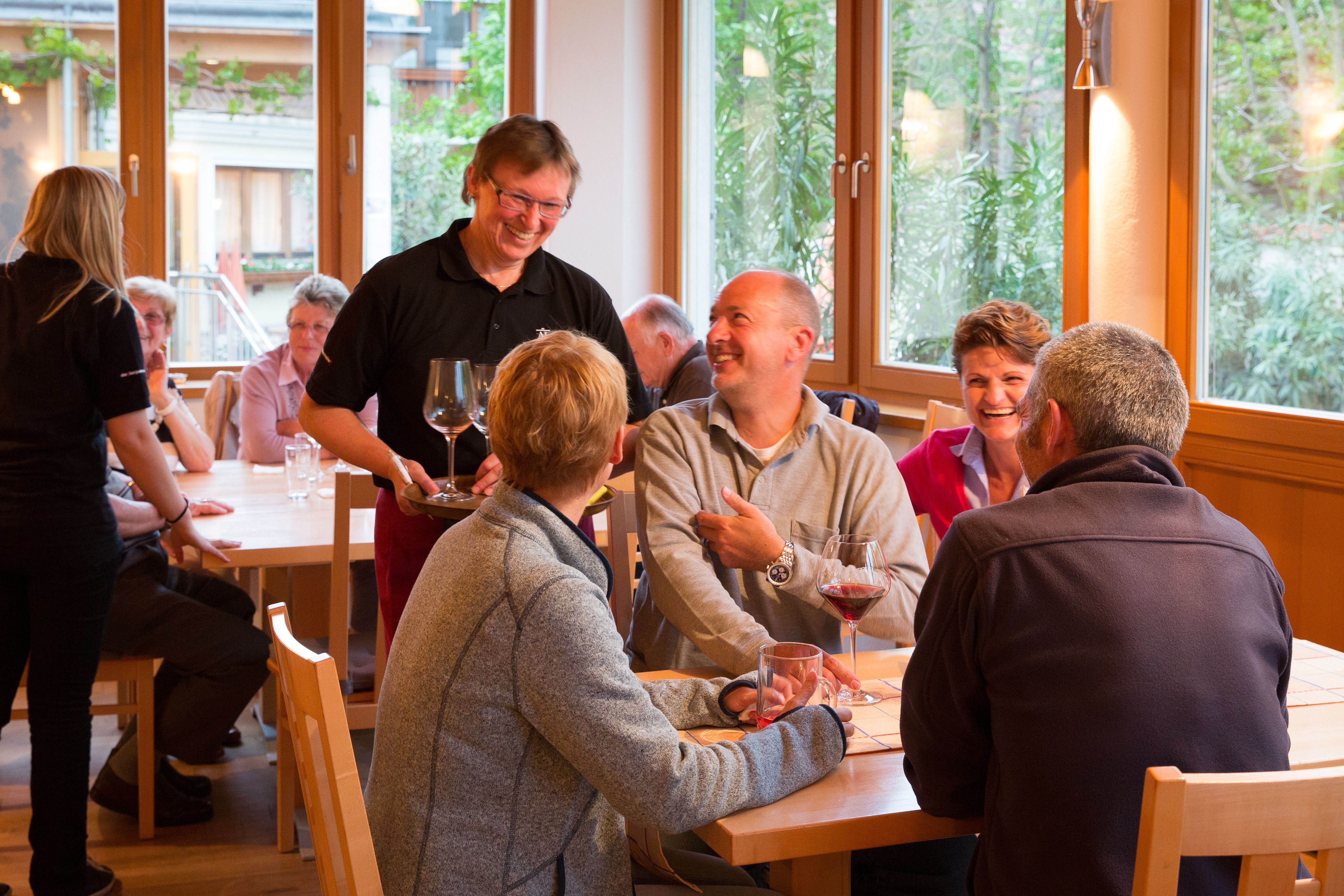 Lidé v útulné restauraci, popíjejí víno a smějí se.