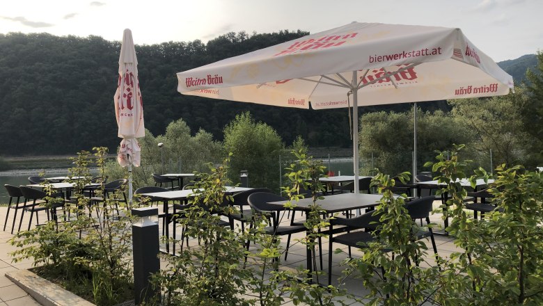 Terasa se stoly, židlemi a slunečn&iacute;ky, obklopen&aacute; př&iacute;rodou.