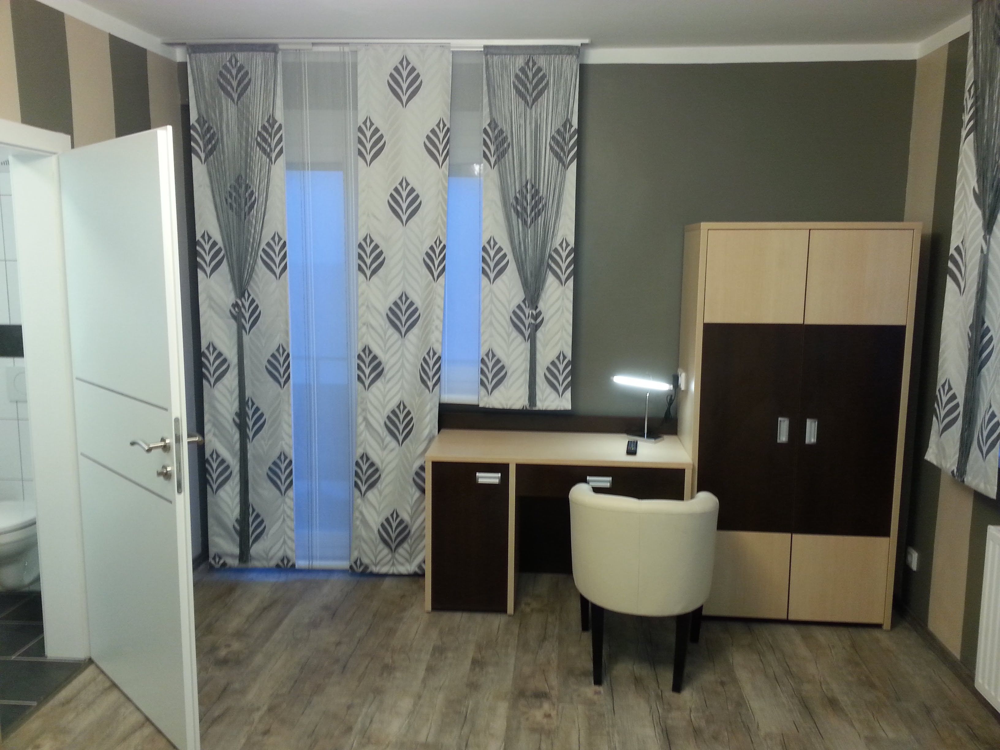Moderní hotelový pokoj se stolem, židlí a šatní skříní.