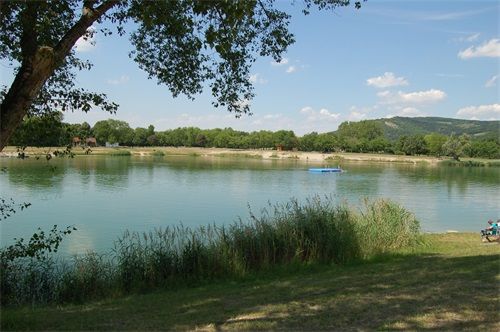 Klidné jezero s rákosím v popředí a zalesněnými kopci v pozadí.