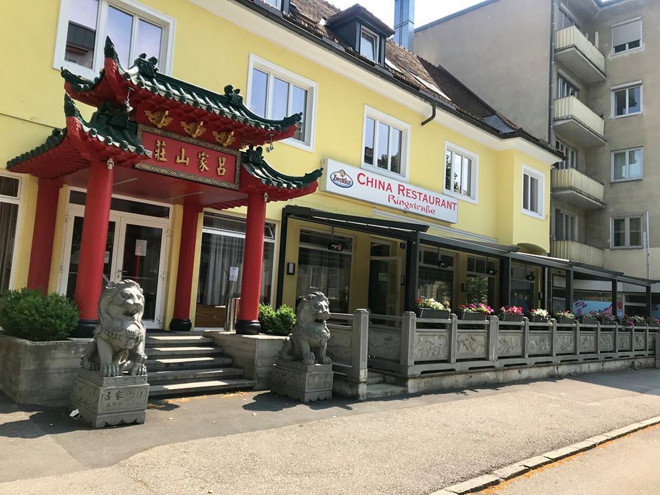 Pohled zvenčí na čínskou restauraci s tradiční bránou a sochami lvů.