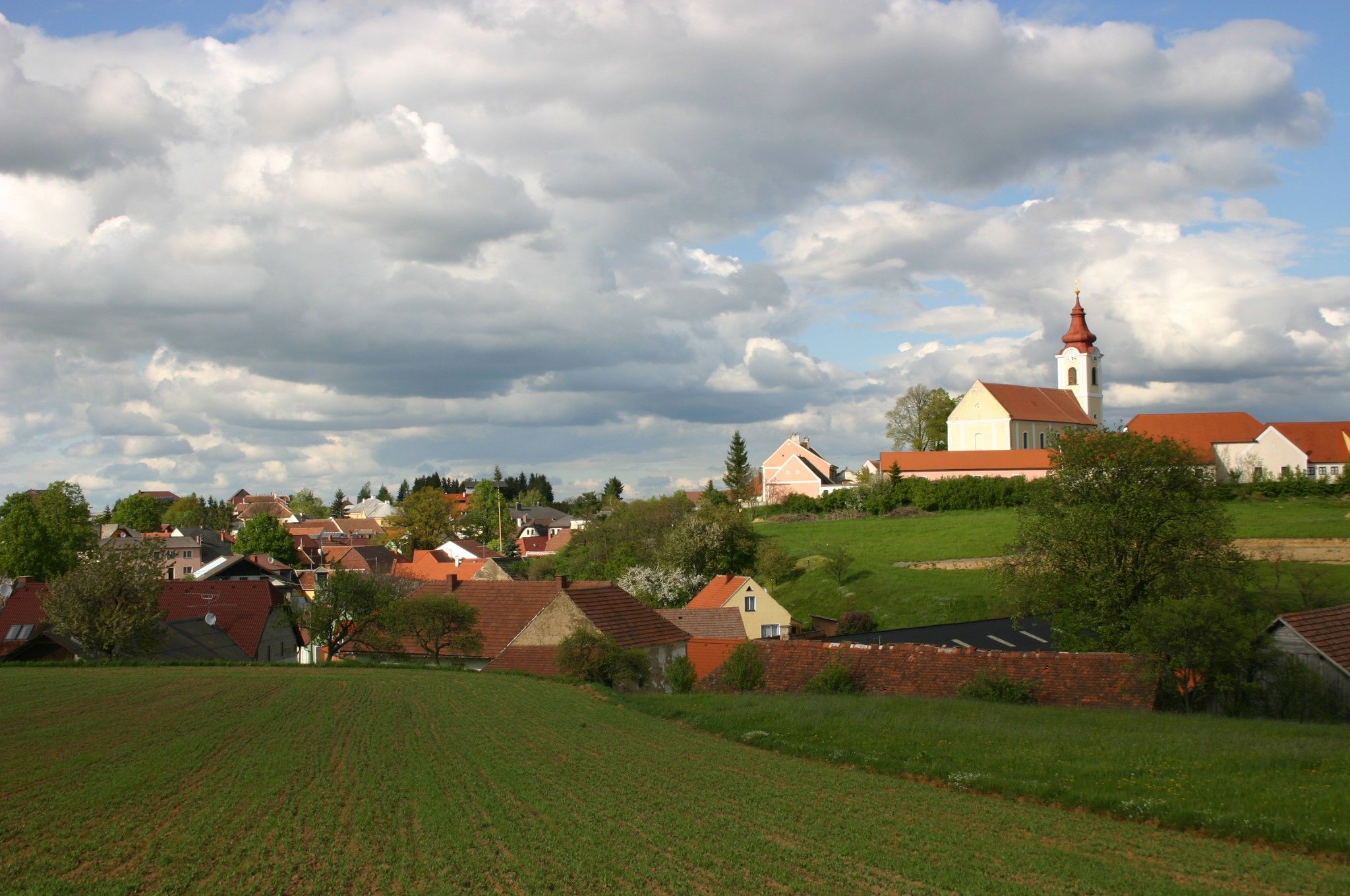 Krajina s vesnicí a kostelem pod zataženou oblohou.