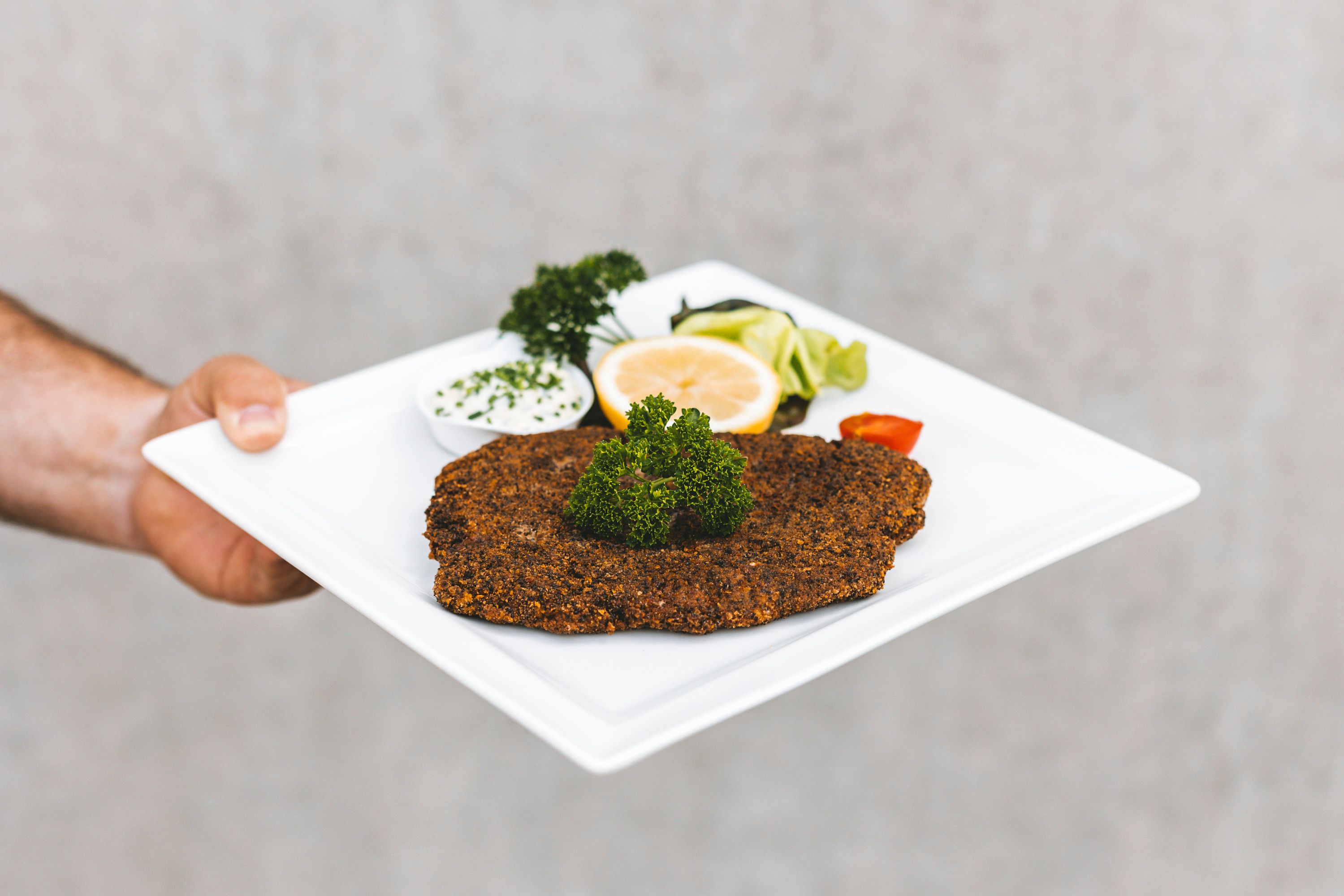 Talíř s obalovanou rybou, citronem, petrželkou a dipem.