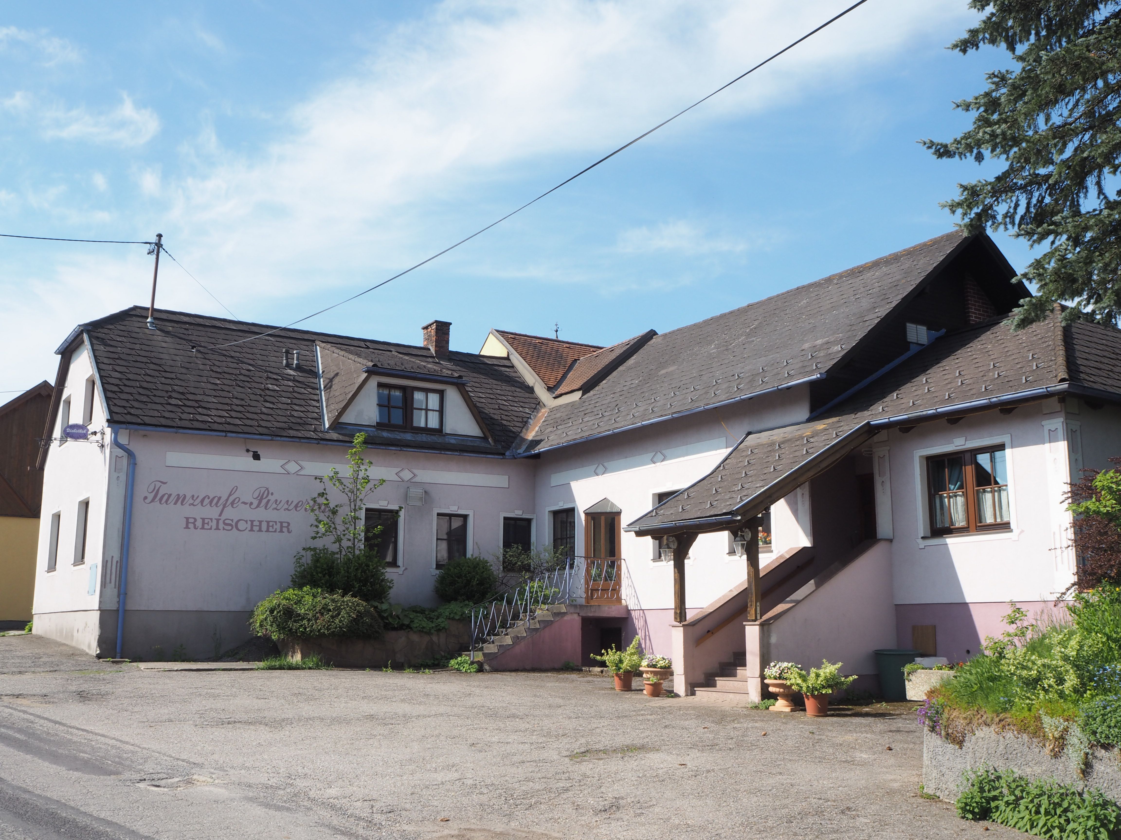 Pohled zvenčí na budovu s nápisem "Tanzcafe-Pizzeria Reischer".