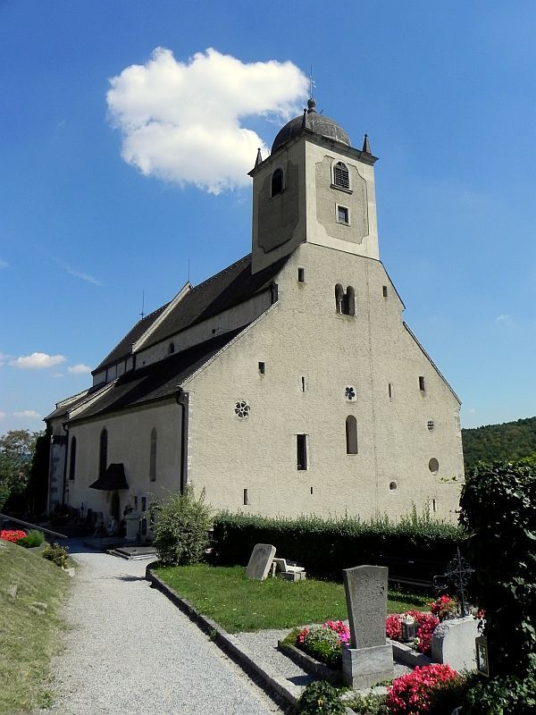 Historický kostel s věží a okolním hřbitovem pod jasnou oblohou.