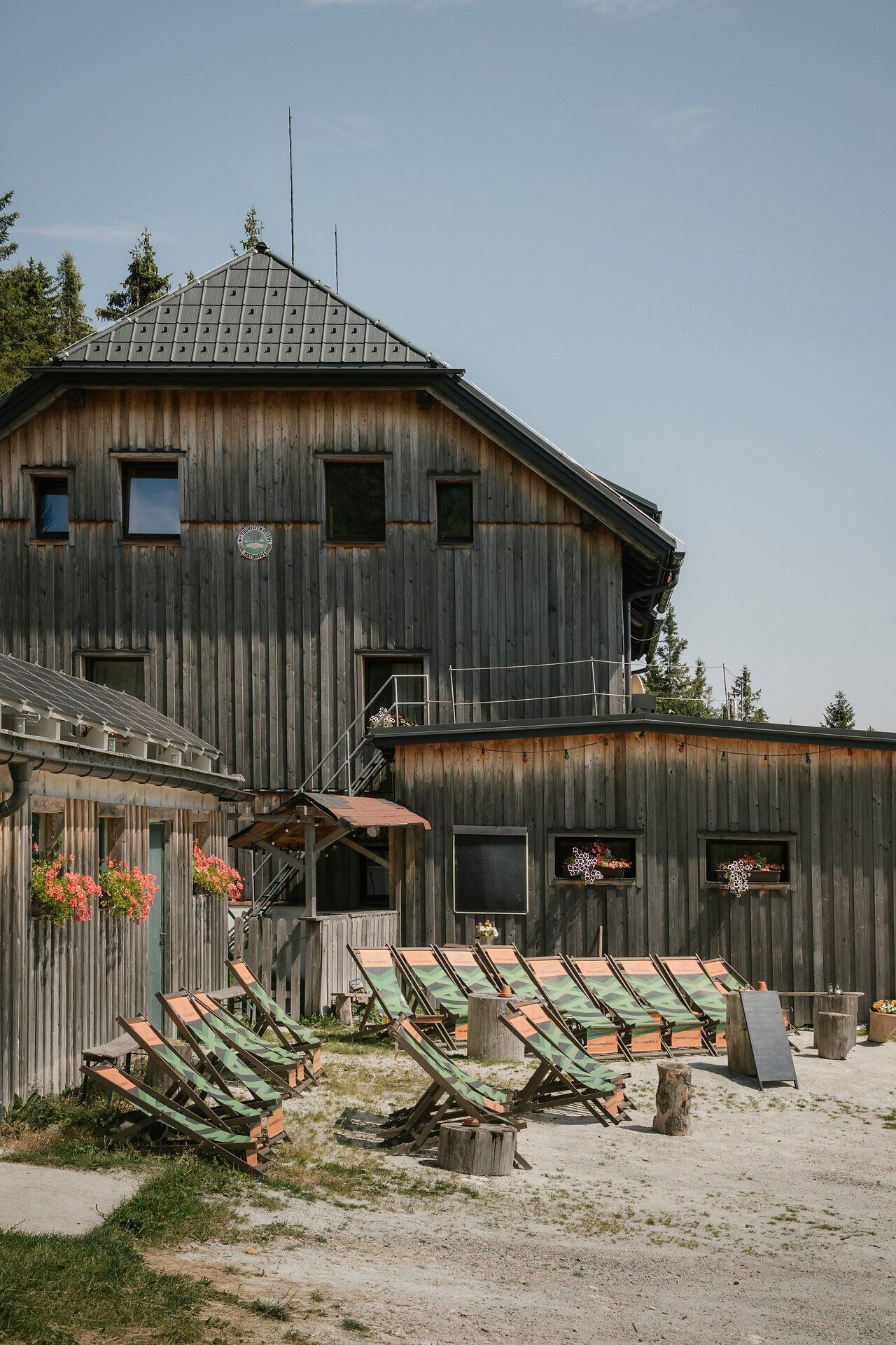 Dům ve stylu „Waxriegelhaus“ na hoře Rax s lehátky před tradiční dřevěnou budovou