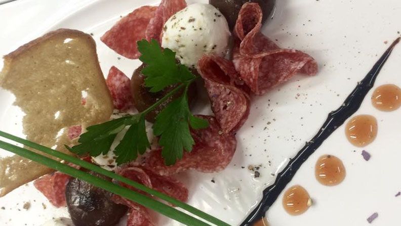 Talíř se salámem, kuličkou kozího sýra, bylinkami a kouskem chleba.