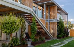 Moderní budova s bílou fasádou a dřevěnými prvky, obehnaná zdí s dřevěnou bránou.