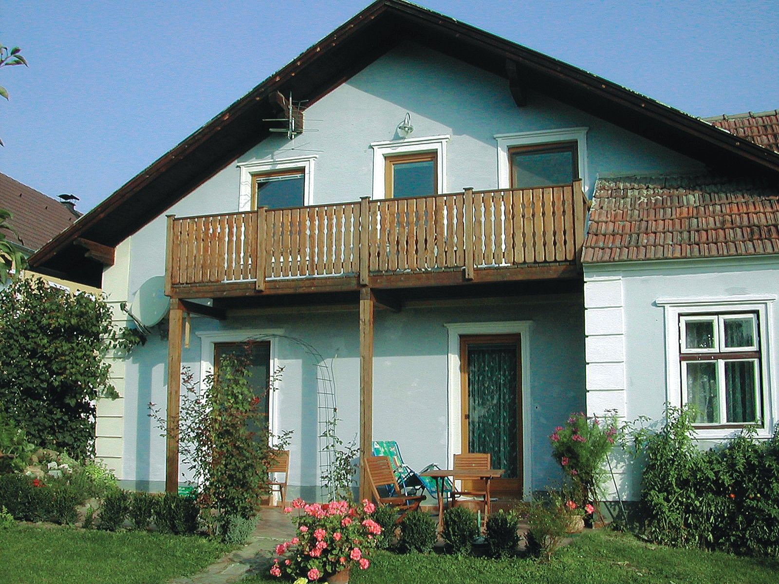 Tradiční vinařský dům s dřevěným balkonem a zahradním nábytkem přede dveřmi.