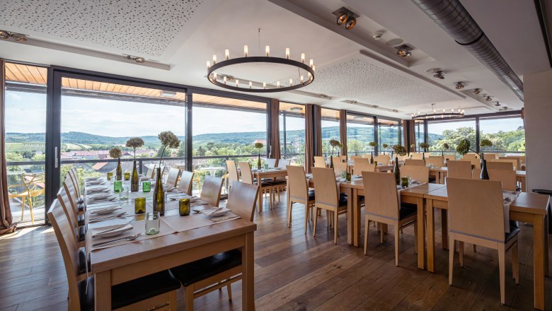 Pohled do interiéru moderní restaurace s velkými okny a výhledem na vinice.