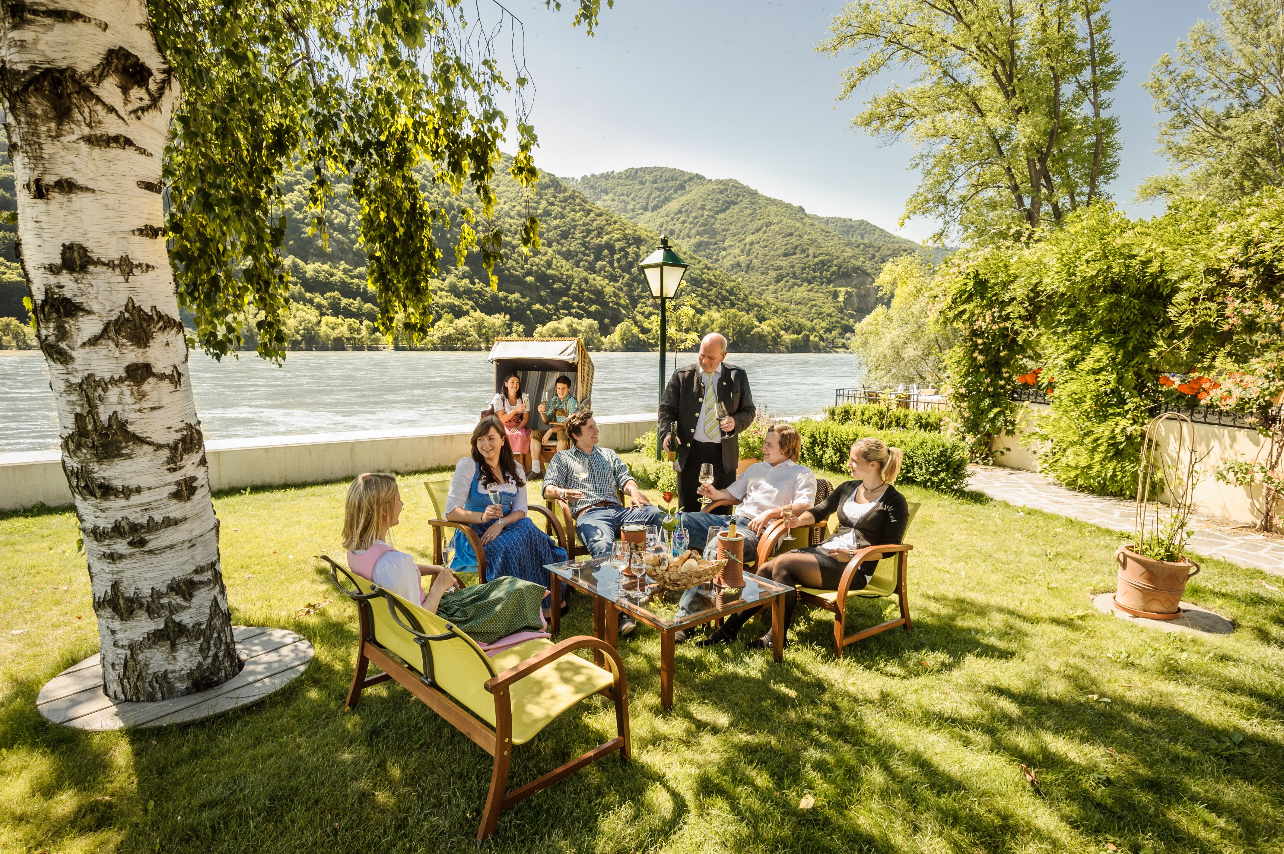 Skupina lidí sedí na zahrádce restaurace na břehu řeky.