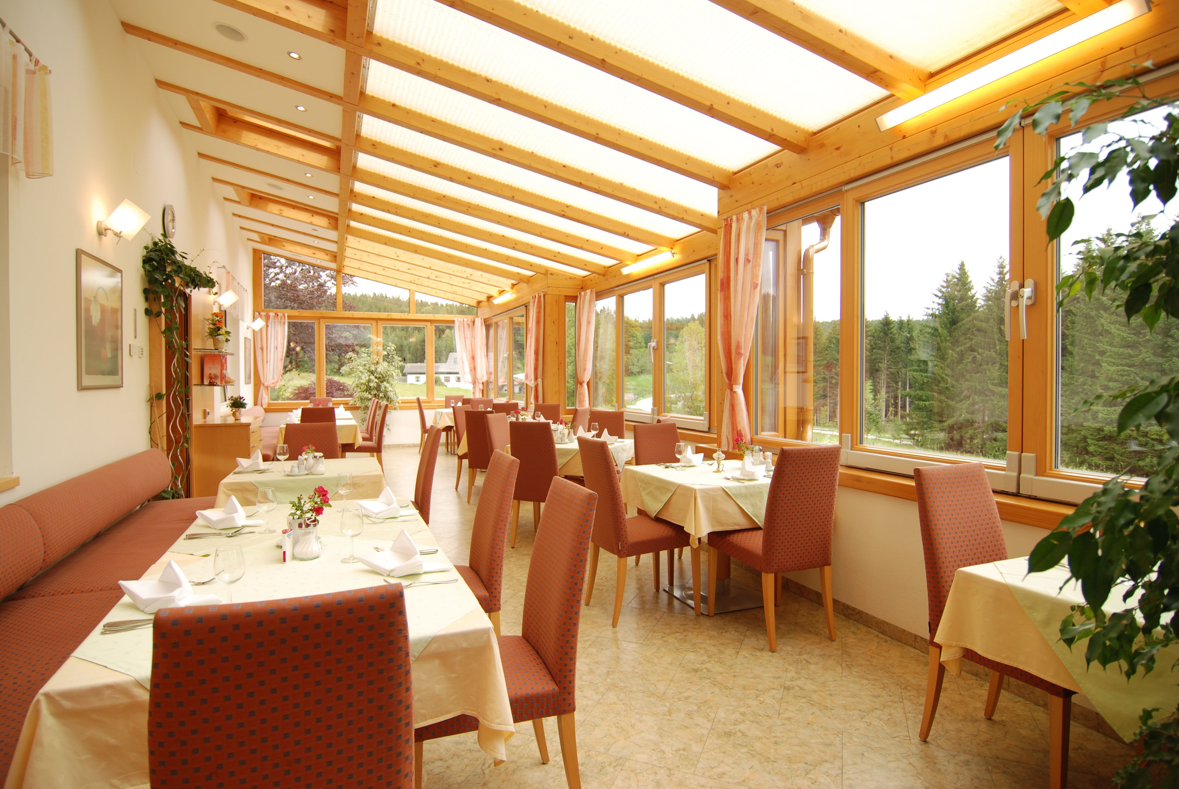 Světlá zimní zahrada restaurace s prostřenými stoly a výhledem na les.