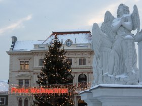 Sv&aacute;tečně vyzdoben&eacute; n&aacute;měst&iacute; se sochou anděla, v&aacute;nočn&iacute;m stromkem a poh&aacute;dkov&yacute;mi svět&yacute;lky s n&aacute;pisem "Merry Christmas".