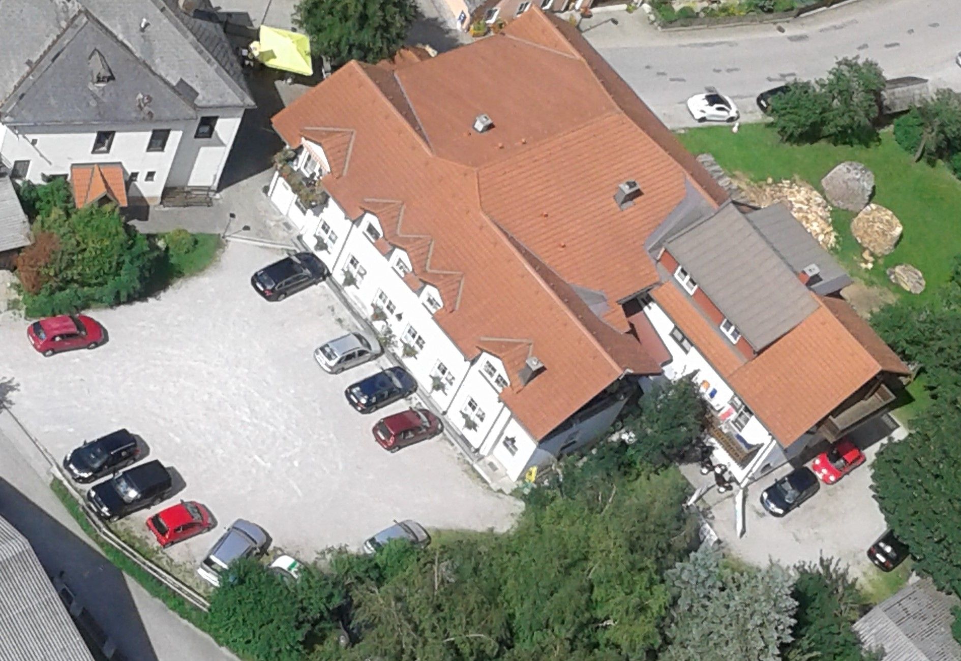 Letecký pohled na komplex budov s červenými střechami a několik zaparkovaných aut na parkovišti.