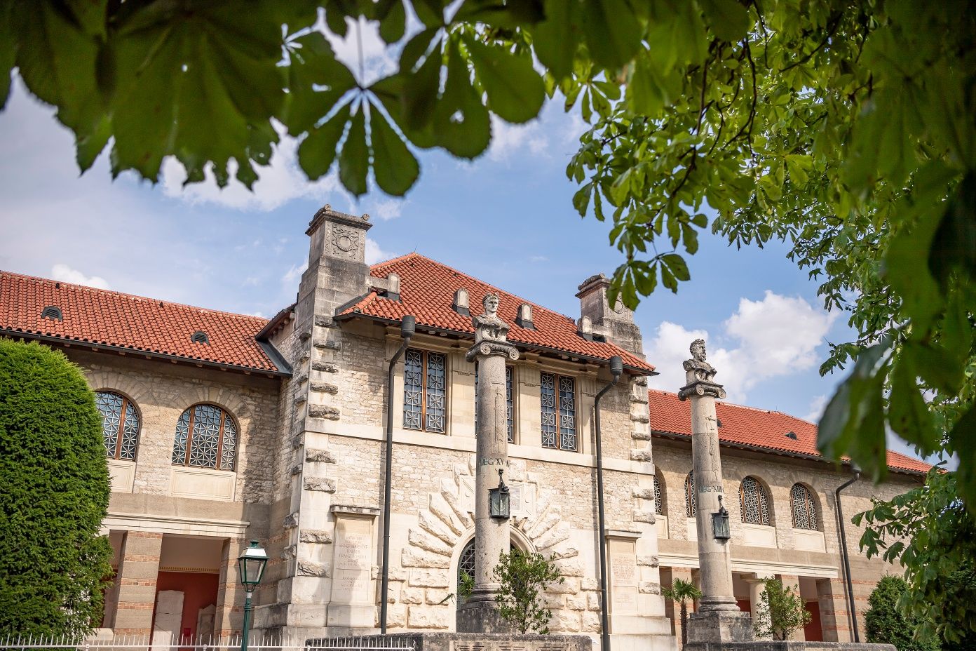 Vnější pohled na muzeum Carnuntinum v Bad Deutsch-Altenburgu se sloupy a červenou taškovou střechou, obklopené zelenými stromy.