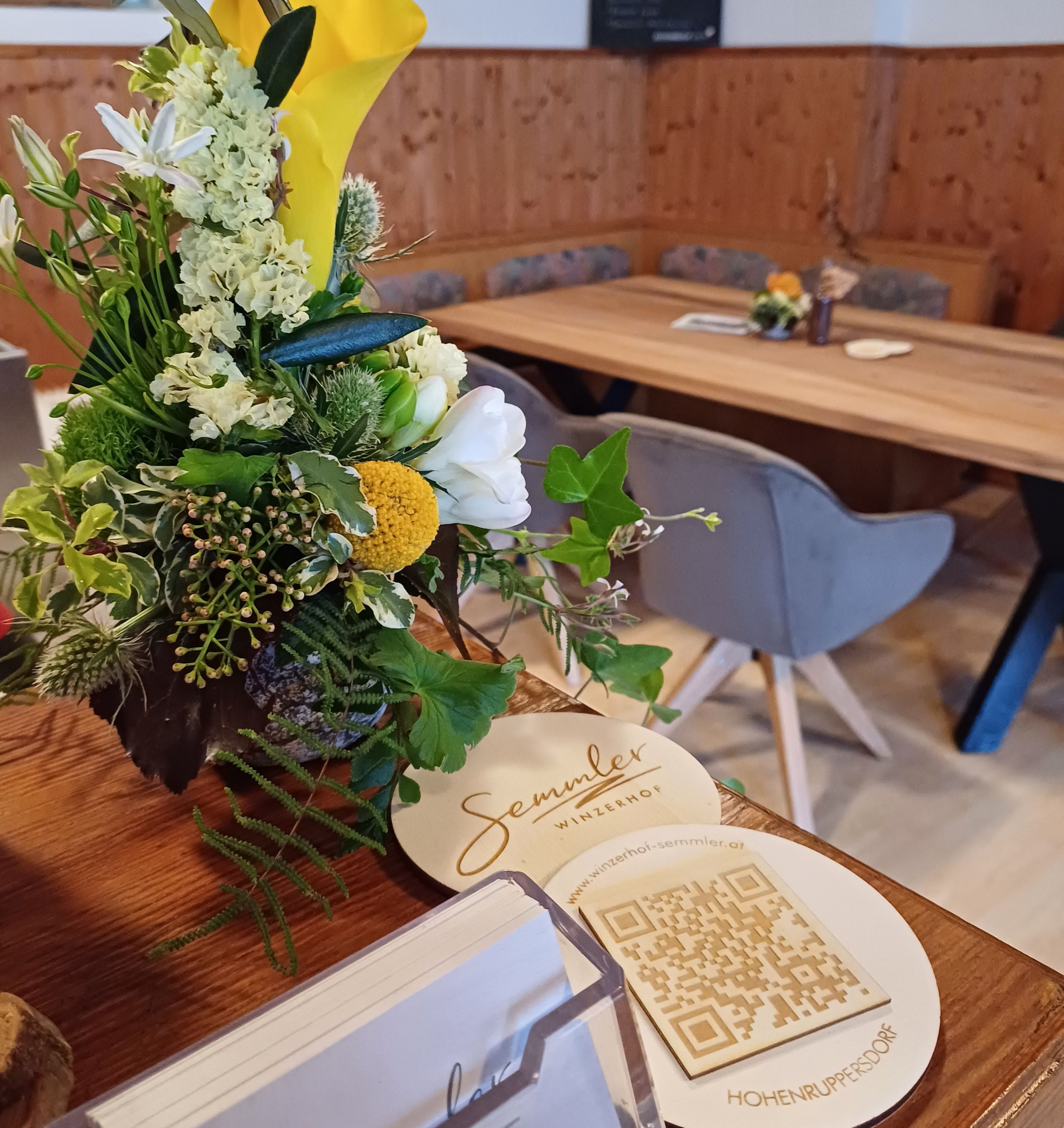 Květinové aranžmá na stole v hotelu Winzerhof Semmler s QR kódem a vizitkami.