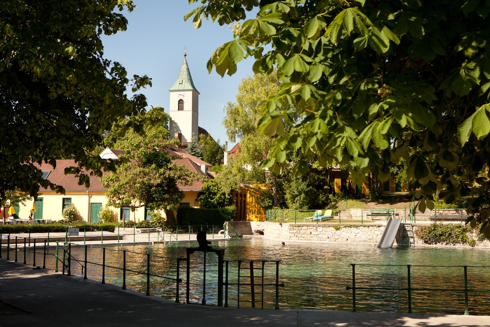 Termální lázně Bad Fischau-Brunn s kostelem v pozadí, obklopené stromy.