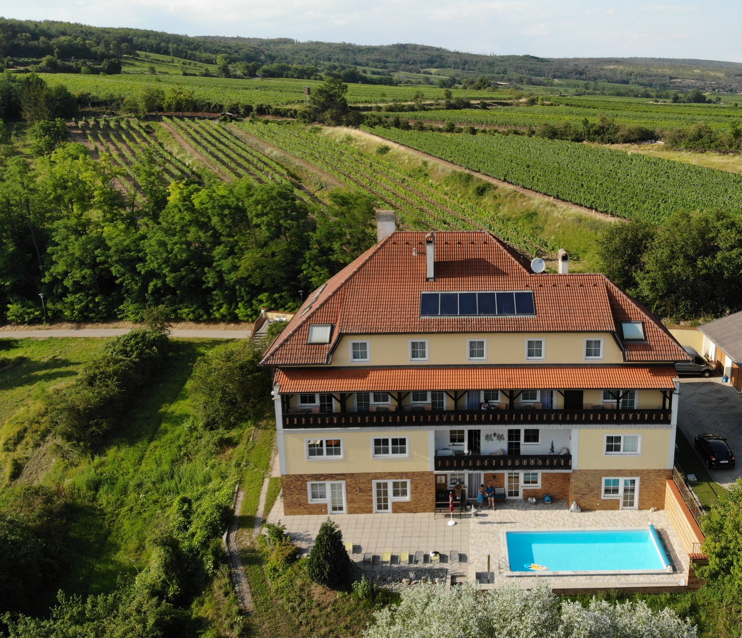 Letecký pohled na velký dům s bazénem a solárními panely, obklopený vinicemi.