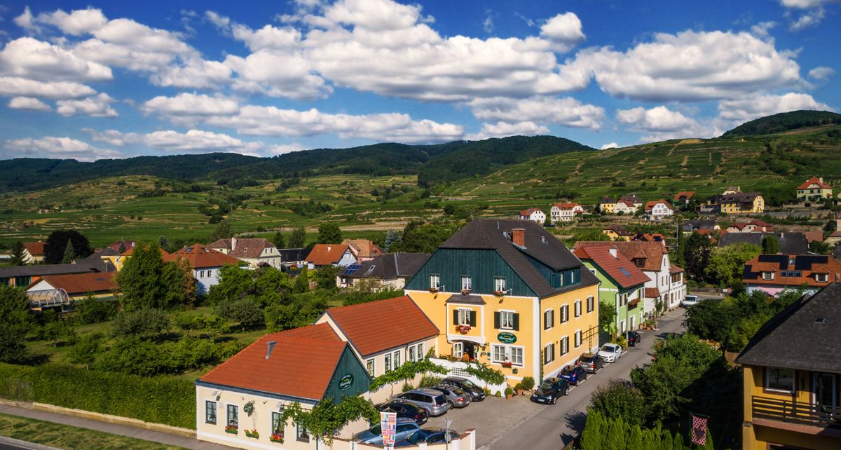Venkovské domy v zelené kopcovité krajině pod modrou oblohou s mraky.