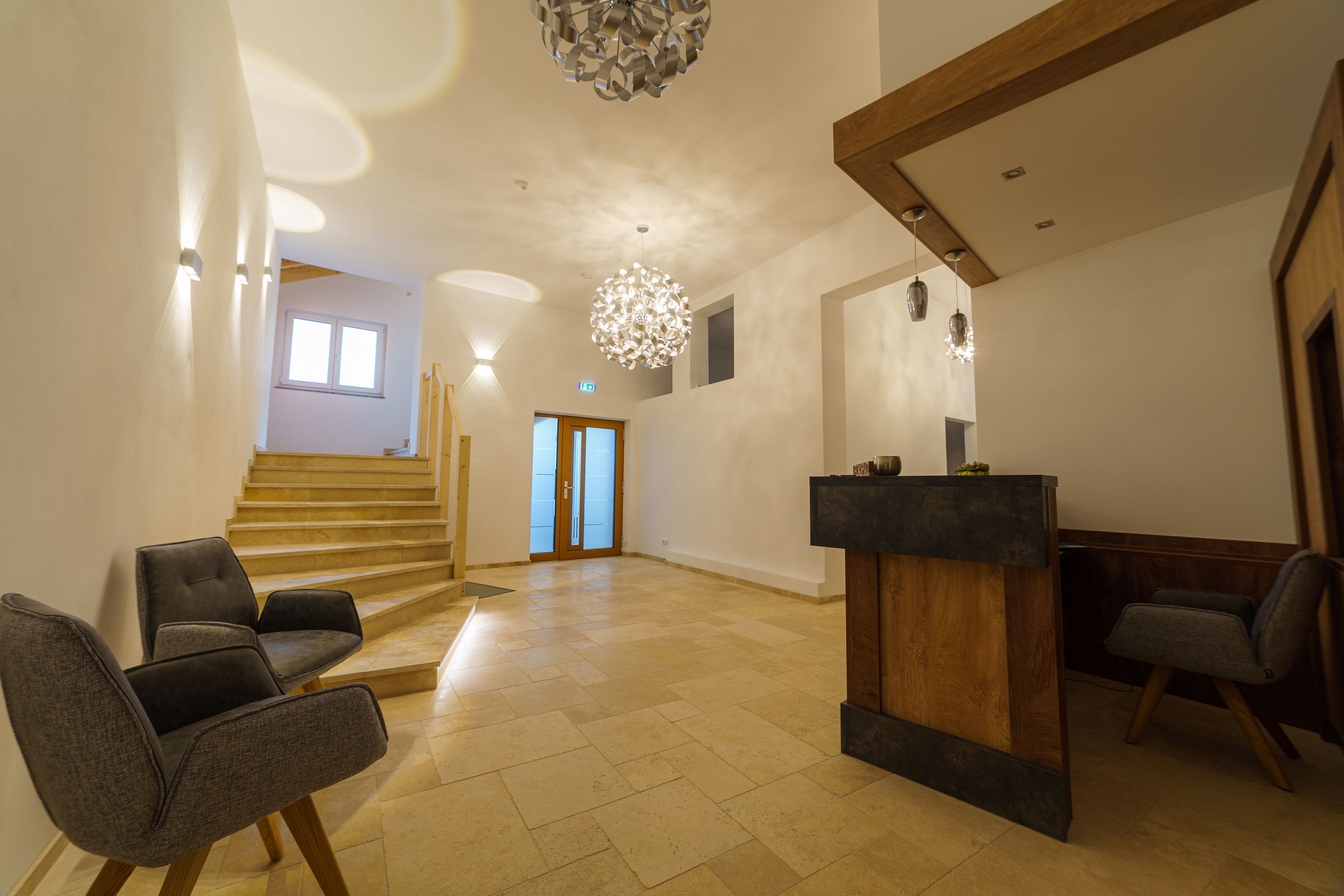 Moderní recepce s dřevěným pultem, dvěma šedými křesly a schody.