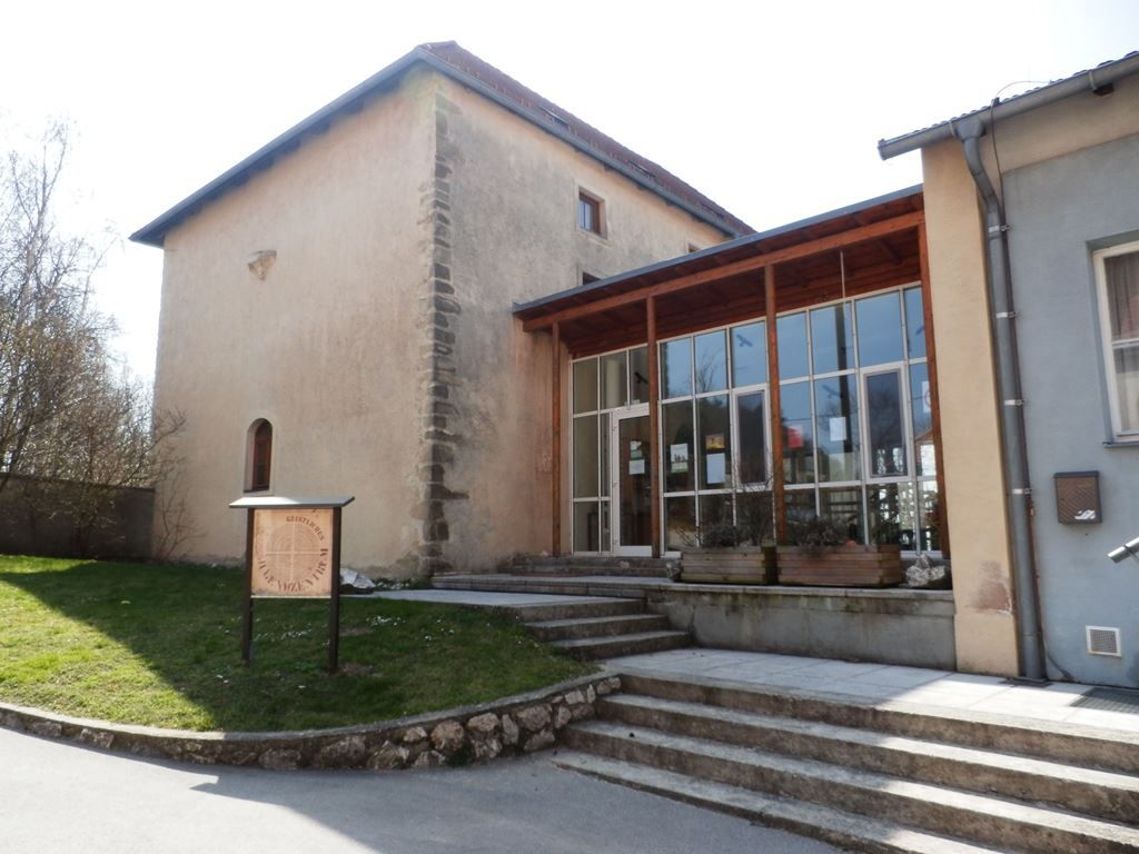 Historická budova s moderní přístavbou a nápisem v popředí.