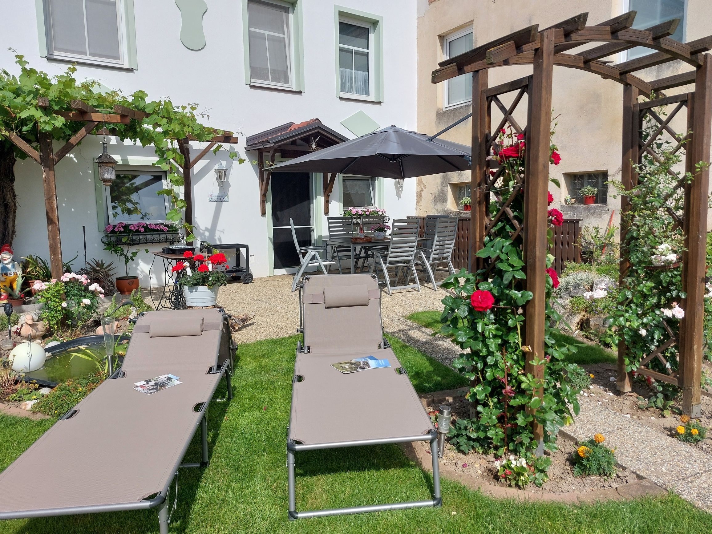 Zahrada s lehátky, pergolou a květinami.