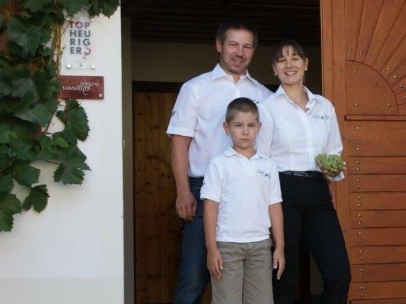 Rodina stojí před budovou s dřevěnými dveřmi, žena drží hrozny.