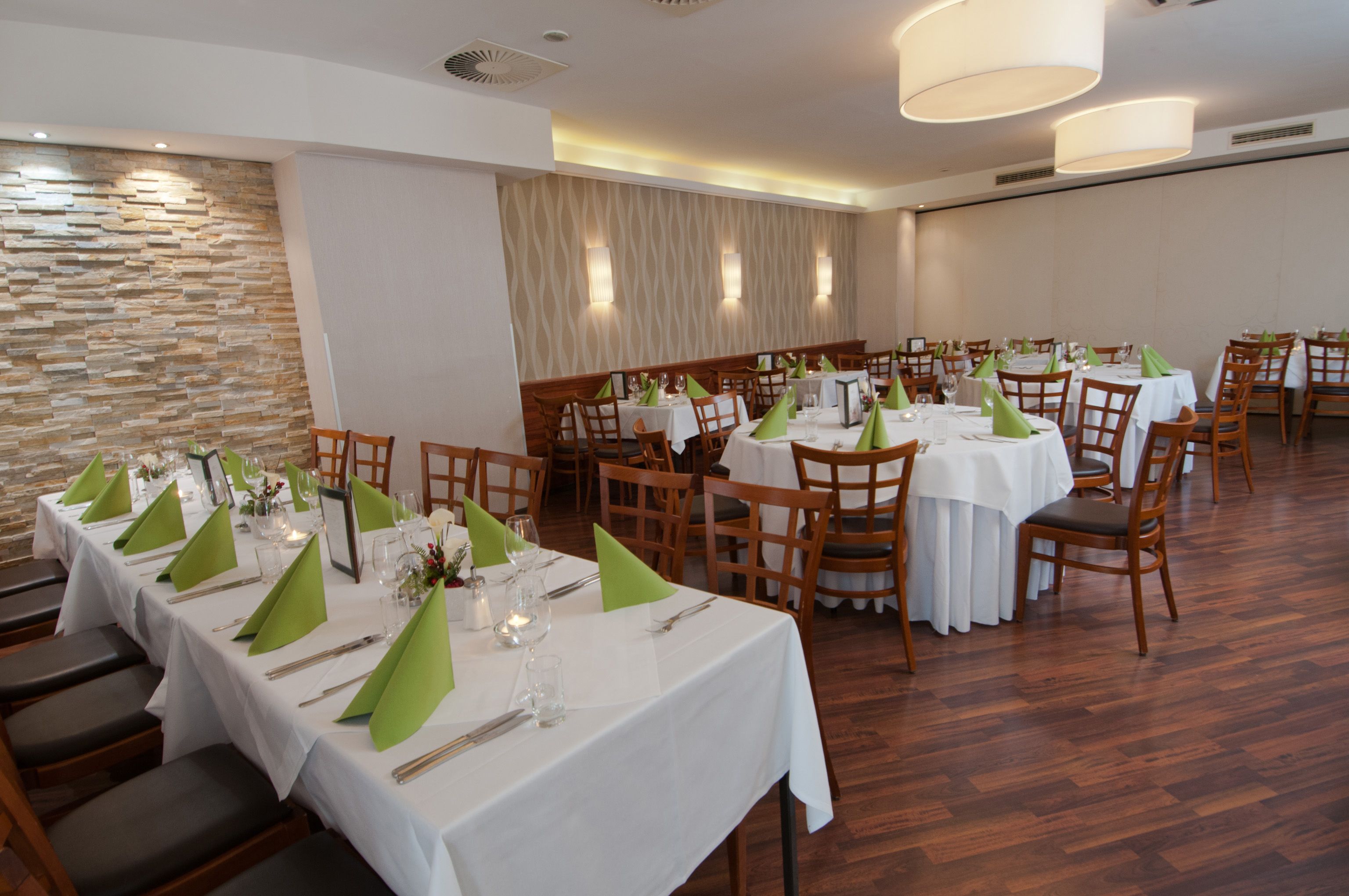 Elegantní restaurace s prostřenými stoly a zelenými ubrousky.