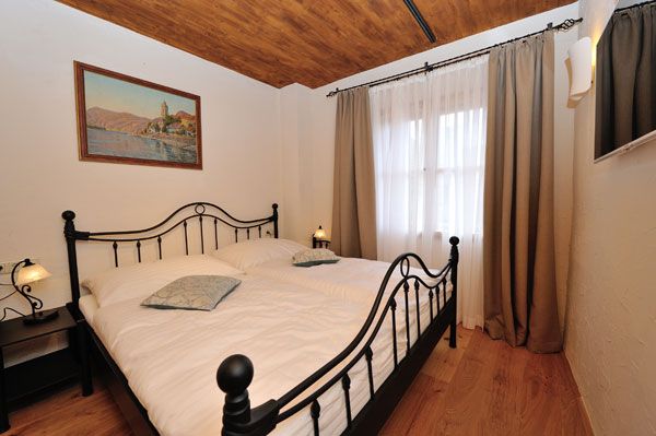 Ložnice s kovovou postelí, dřevěnou podlahou a malbou na stěně.