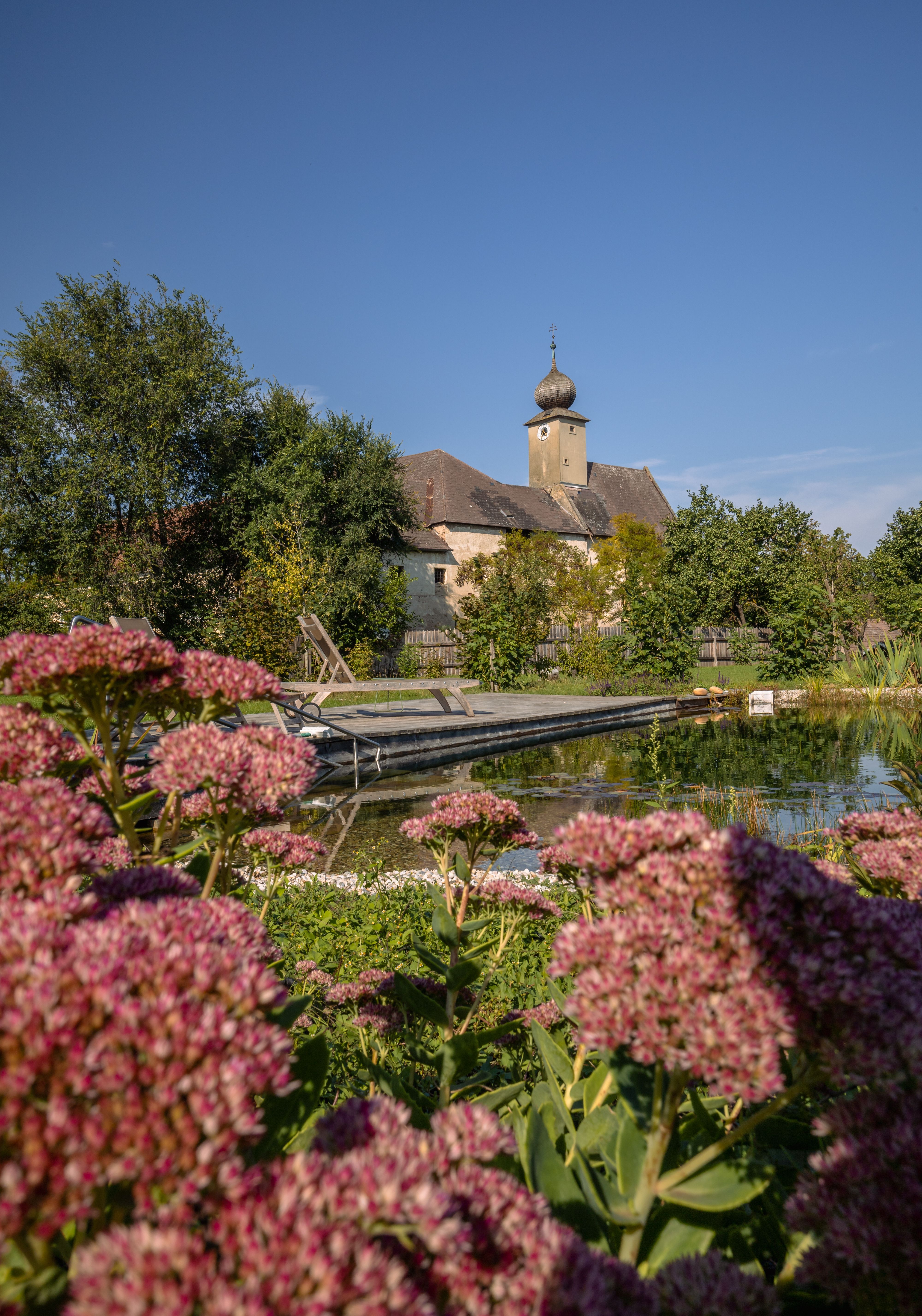 Ložnice s klenutým stropem, dřevěnou podlahou, postelí, křeslem, komodou a kožešinovým kobercem.
