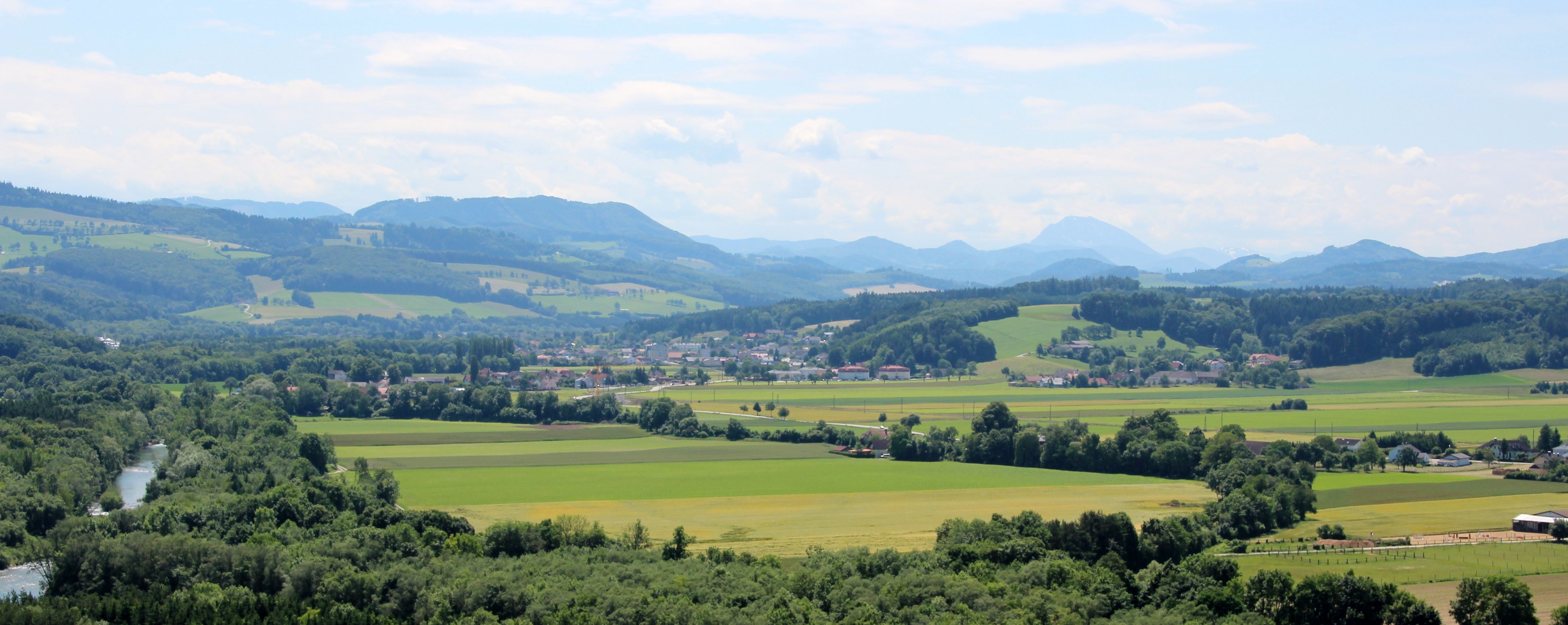 Panorama zelené krajiny s kopci, poli a řekou.
